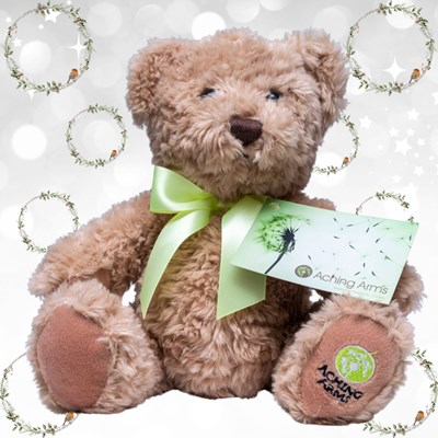 An Aching Arms Comfort Bear with a grey christmas themed background with green christmas wreaths